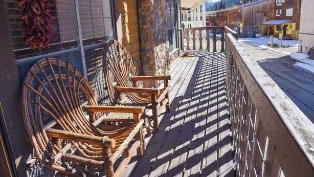 Eine Holzterrasse mit zwei Korbstühlen, einer Steinpfeiler und Blick auf eine verschneite Straße und Häuser.