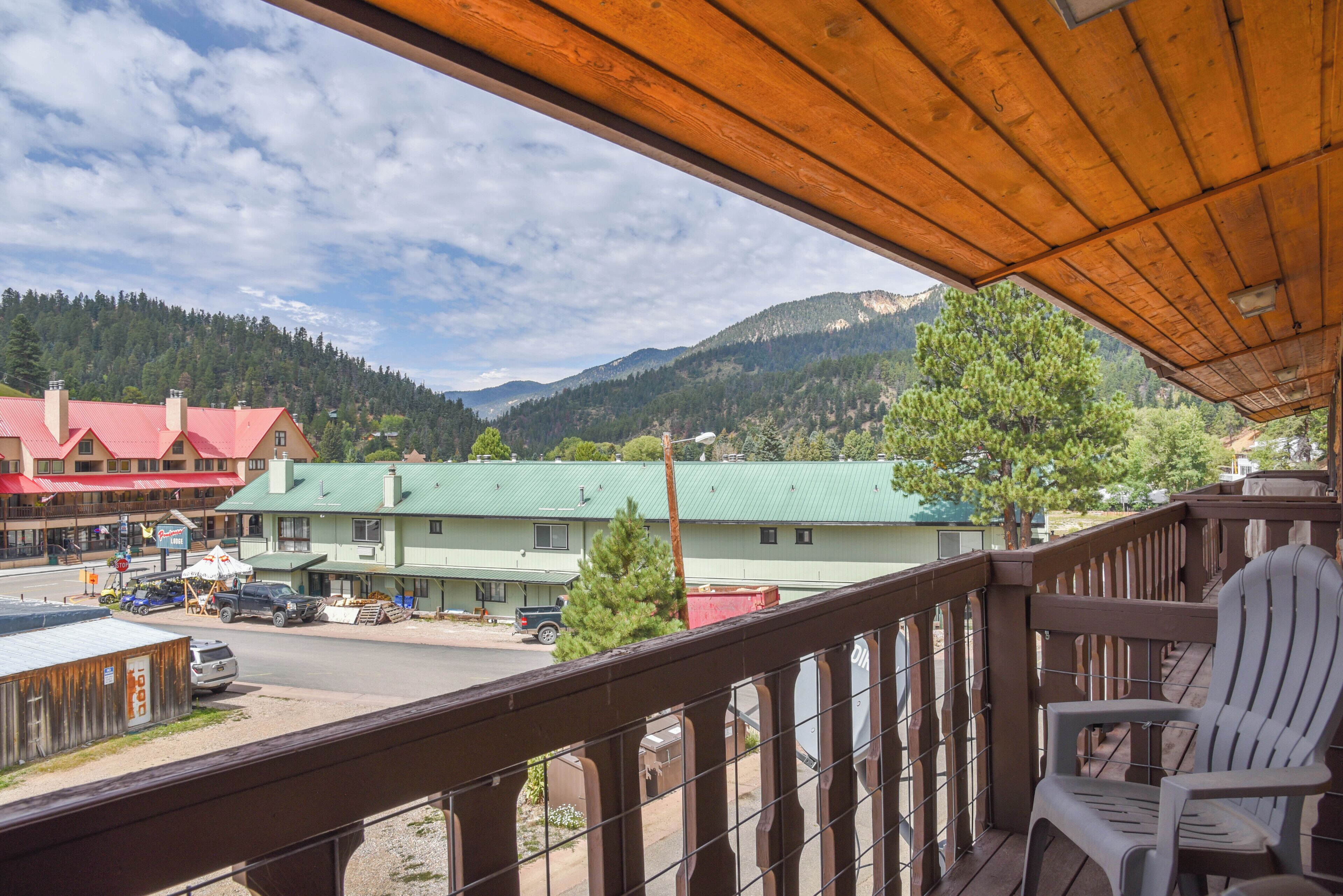 A balcony with a view of a town, a green building, and mountains in the background.