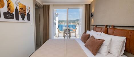 A hotel room with a large bed, a balcony with a table and chairs, and a view of the sea.