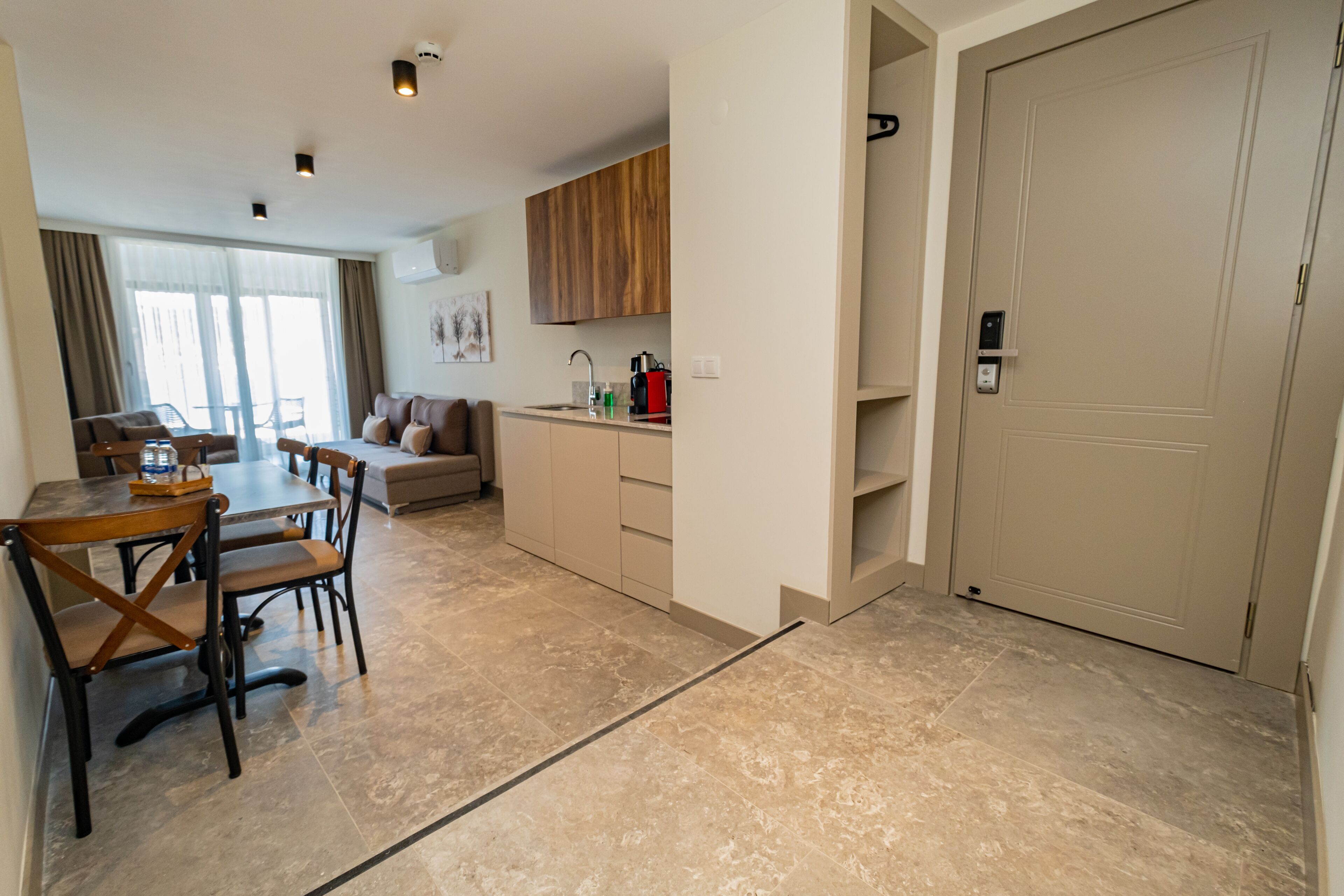 A modern hotel room with a dining area, kitchenette, and a large door.