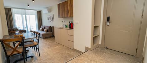 A modern hotel room with a dining area, kitchenette, and a large door.