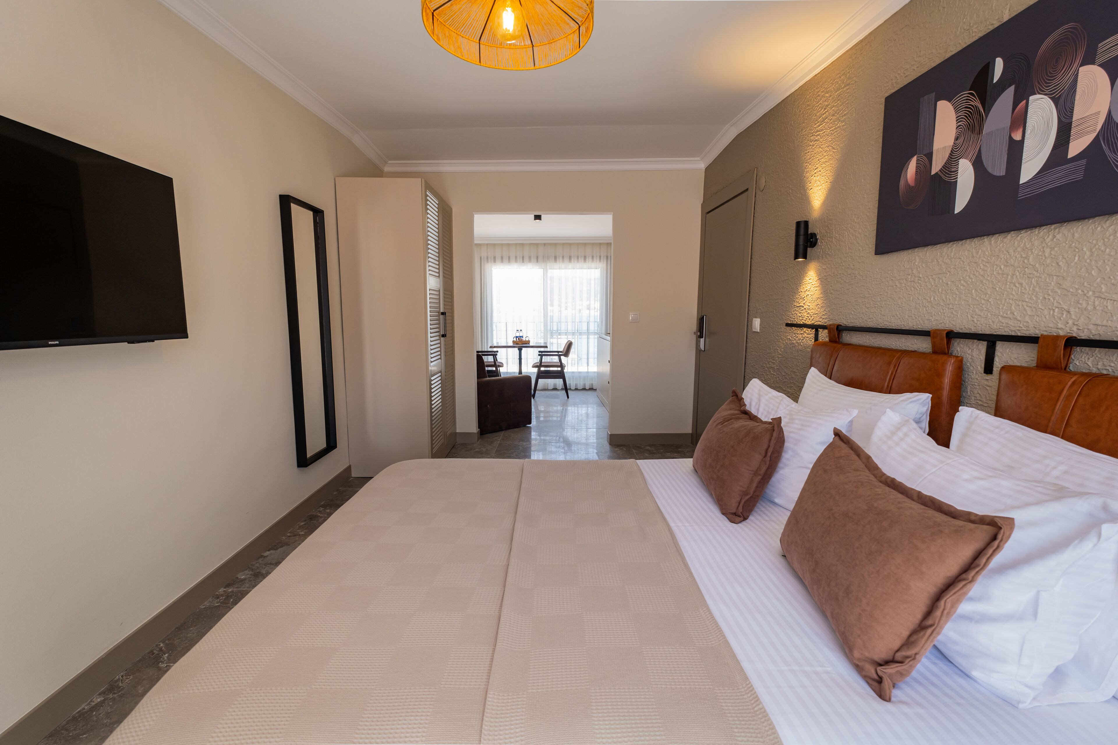 A hotel room with a large bed, a flat-screen TV mounted on the wall, a dining area in the background, and a modern art piece on the wall.