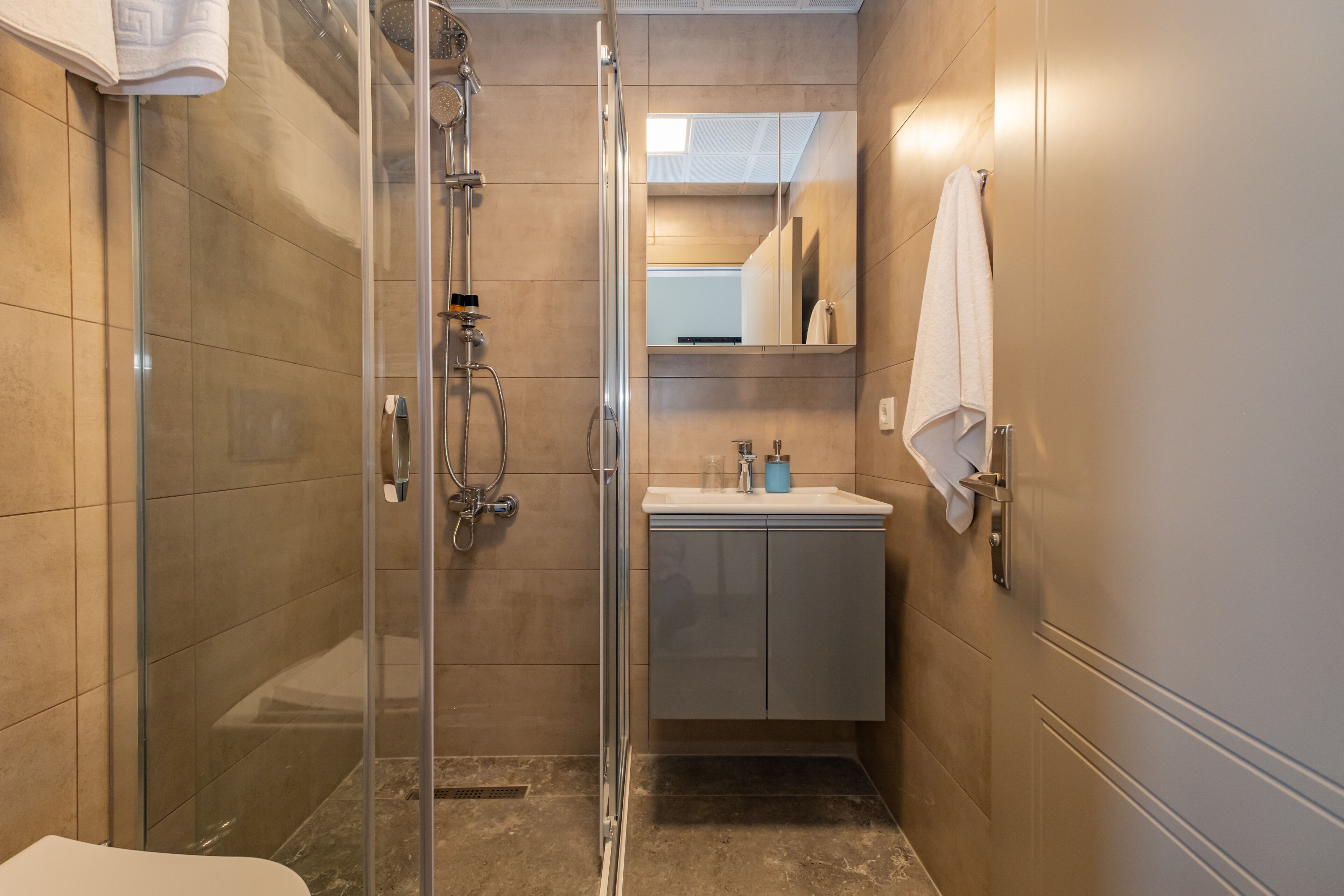 Un baño moderno con cabina de ducha de vidrio, un lavamanos blanco y un espejo sobre él.