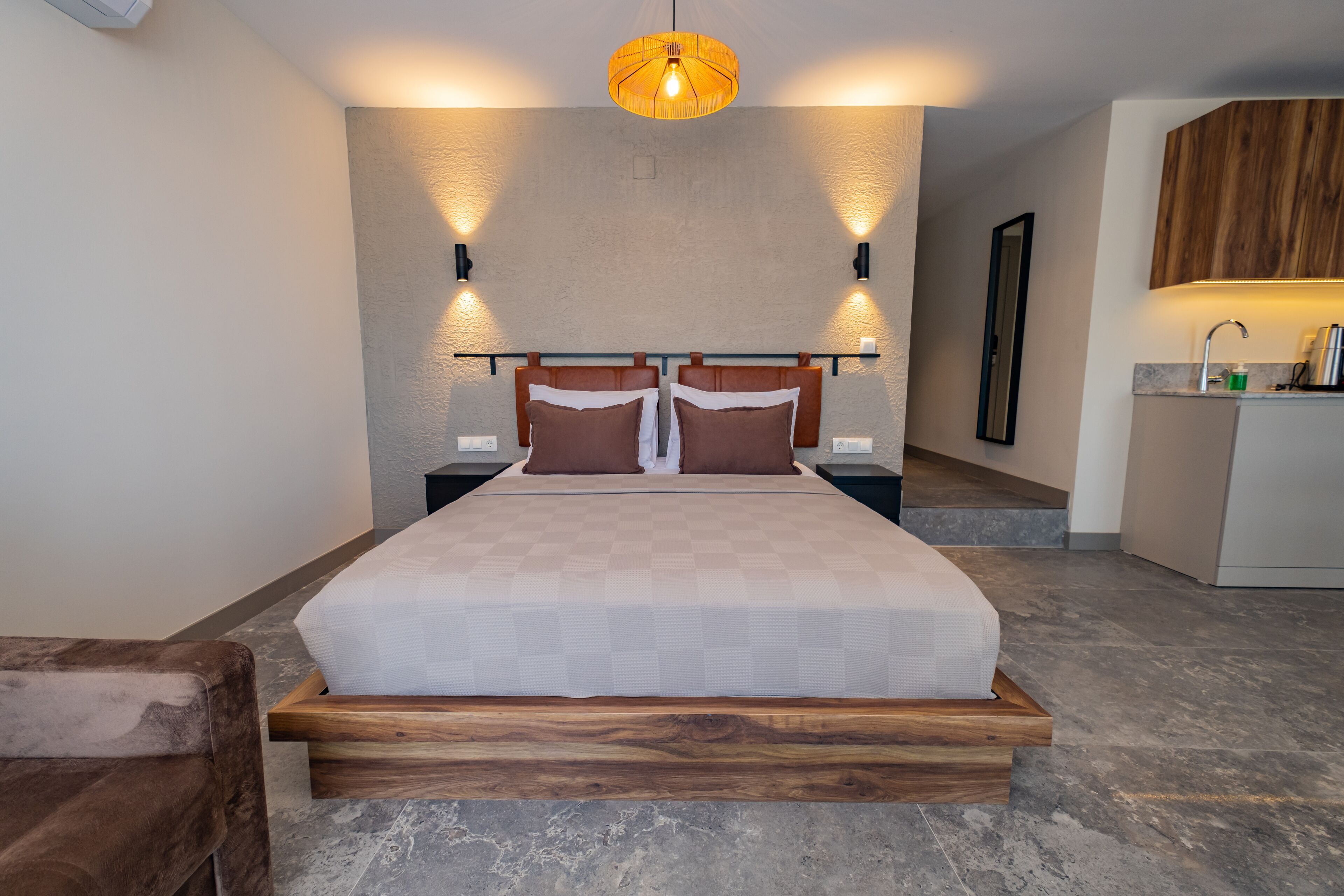 A modern bedroom with a large bed, wooden headboard, and two wall-mounted lights.