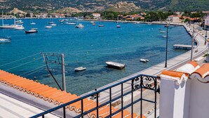 A coastal town with boats docked at a marina, a promenade, and buildings in the background.
