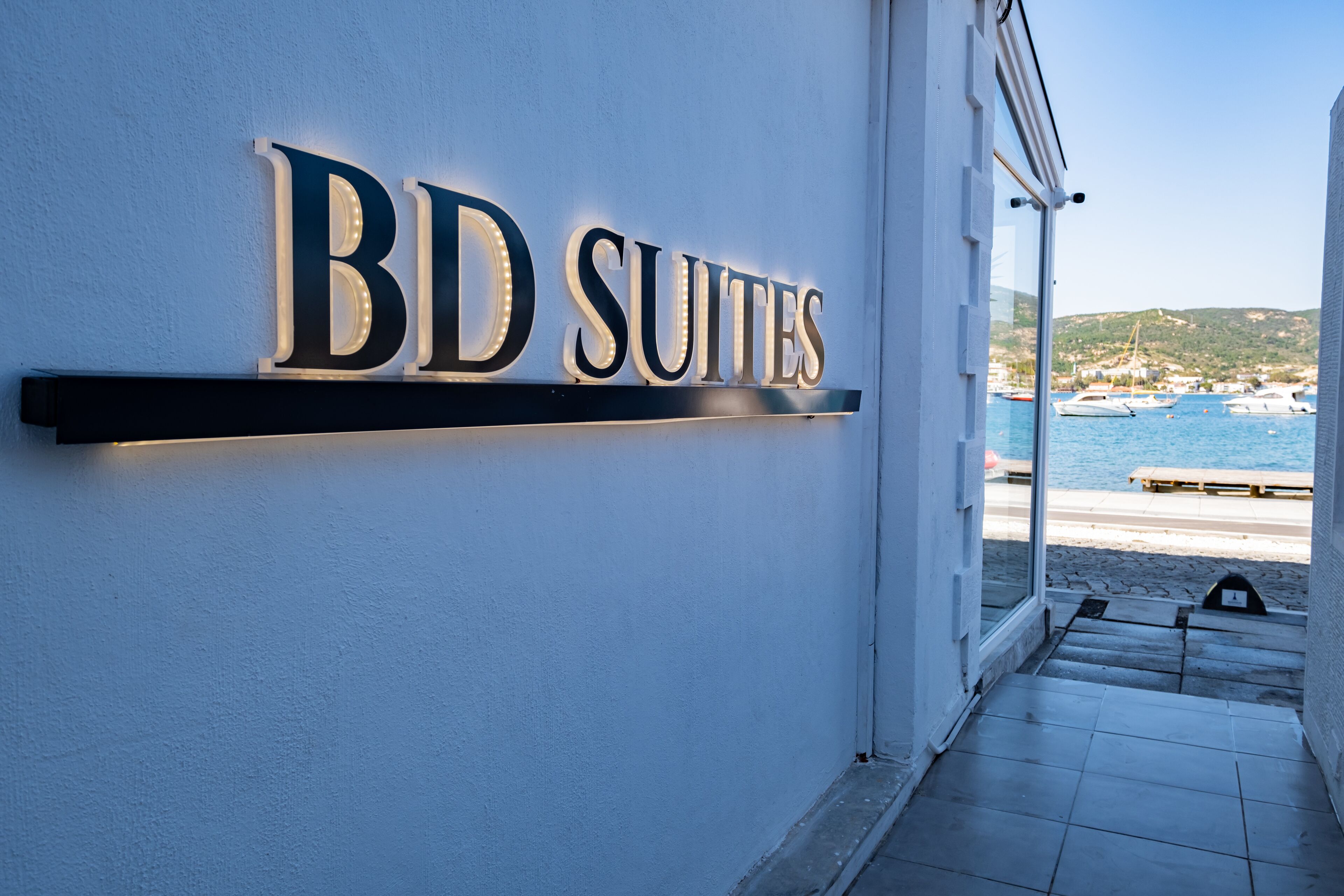 Une enseigne indiquant « BD SUITES », avec en arrière-plan une plage et des bateaux.