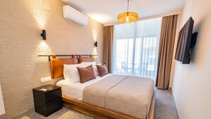 A modern hotel room with a large bed, a nightstand, a flat-screen TV, and a view of the outdoors.