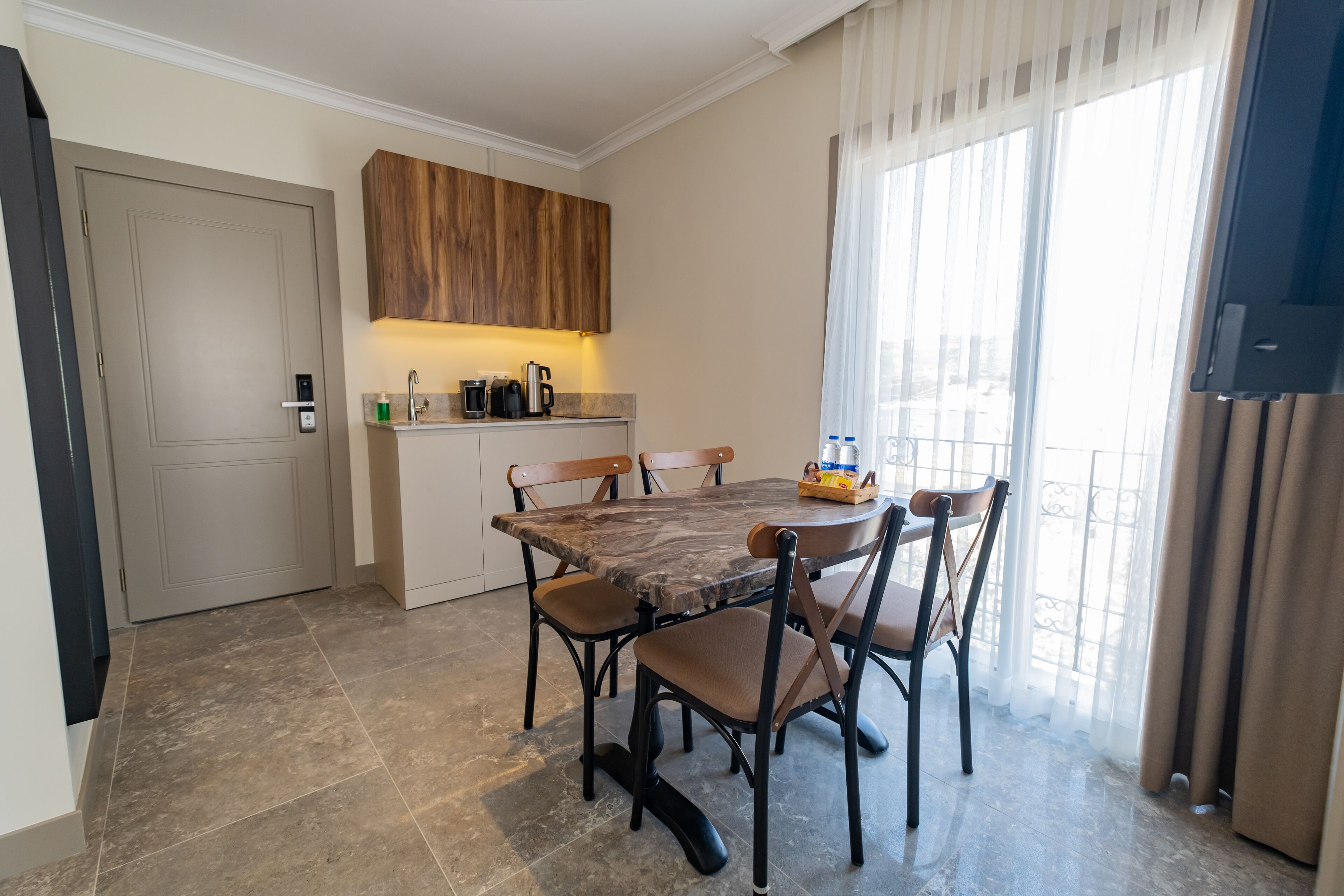Una cocina compacta con zona de comedor, que incluye una mesa de mármol, sillas de madera y un horno empotrado.