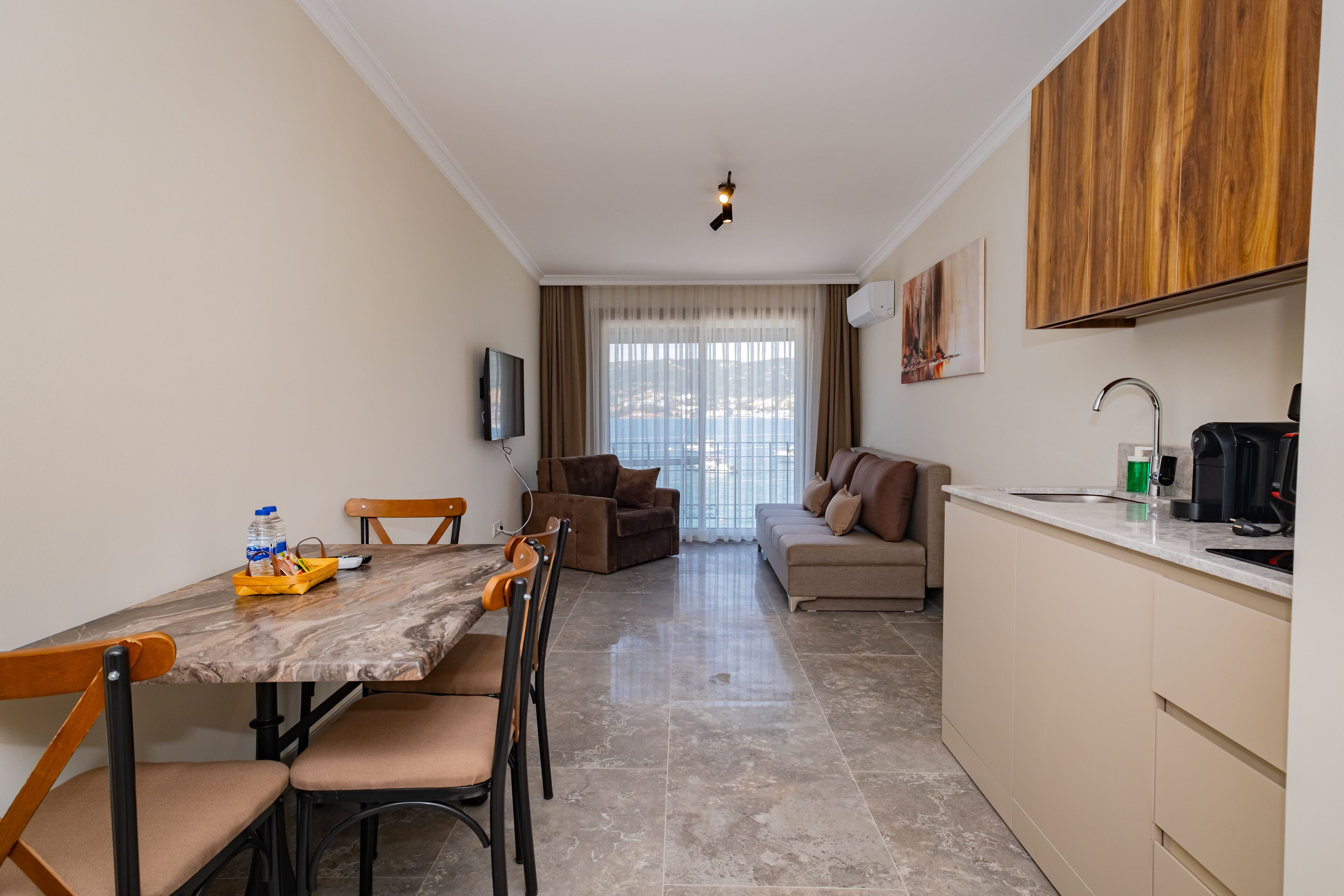 A modern living room with a dining area, a sofa, a kitchen with a sink, and a television mounted on the wall.