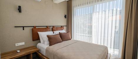 Una habitación de hotel moderna con una cama grande, una mesita de noche, aire acondicionado en la pared y un ventanal con cortinas.