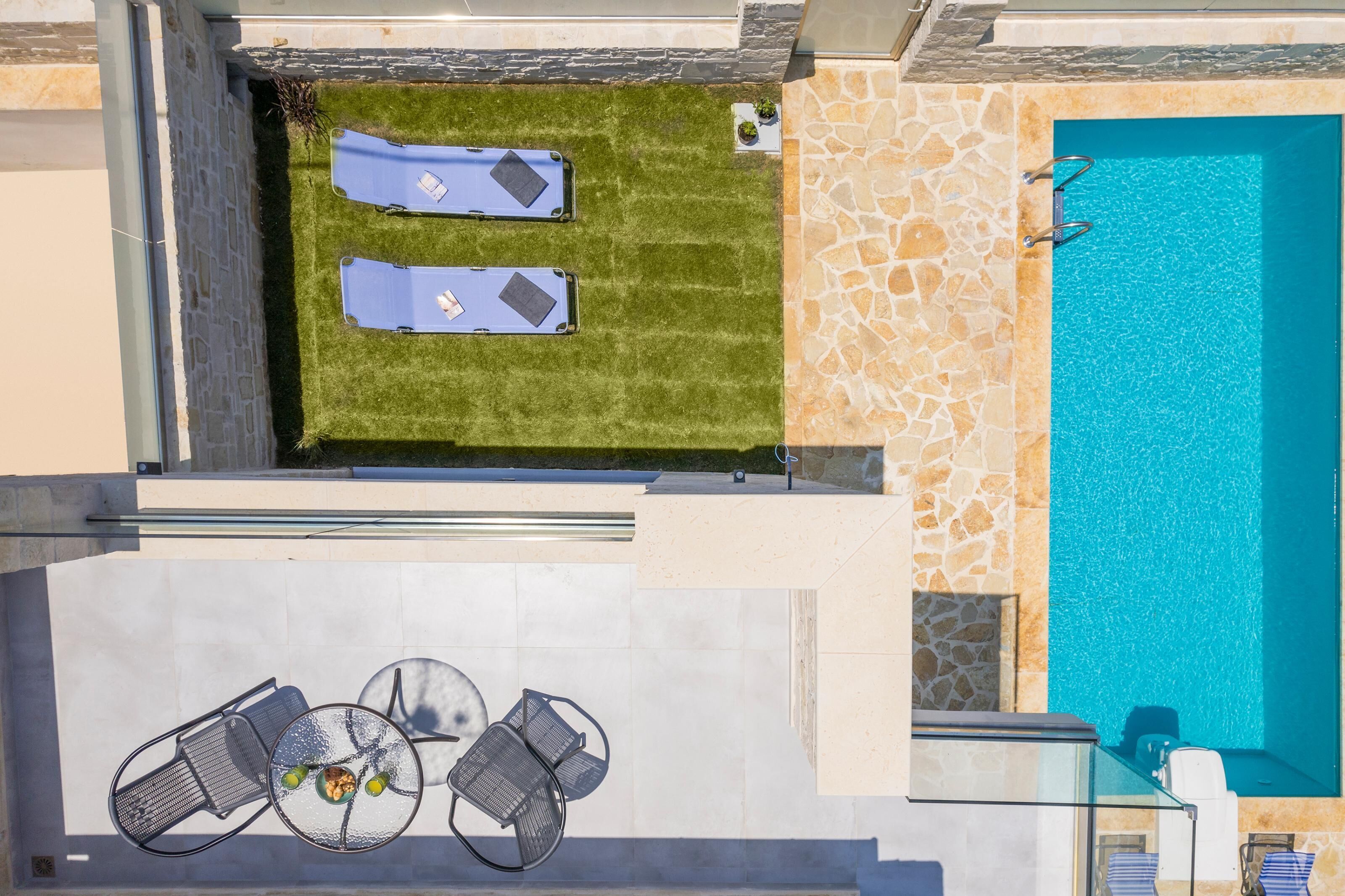 A rooftop pool area with two sun loungers, a table with chairs, and a clear blue pool.