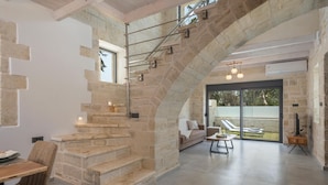 A modern interior with a stone staircase, a sofa, and a dining area. - Villa Megalith (Chania)