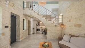 A spacious living area with a stone wall, a wooden coffee table, a sofa, and a staircase leading to an upper level. - Villa Megalith (Chania)