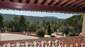 Un balcon offrant une vue sur un paysage montagneux, un sol carrelé et une balustrade décorative.