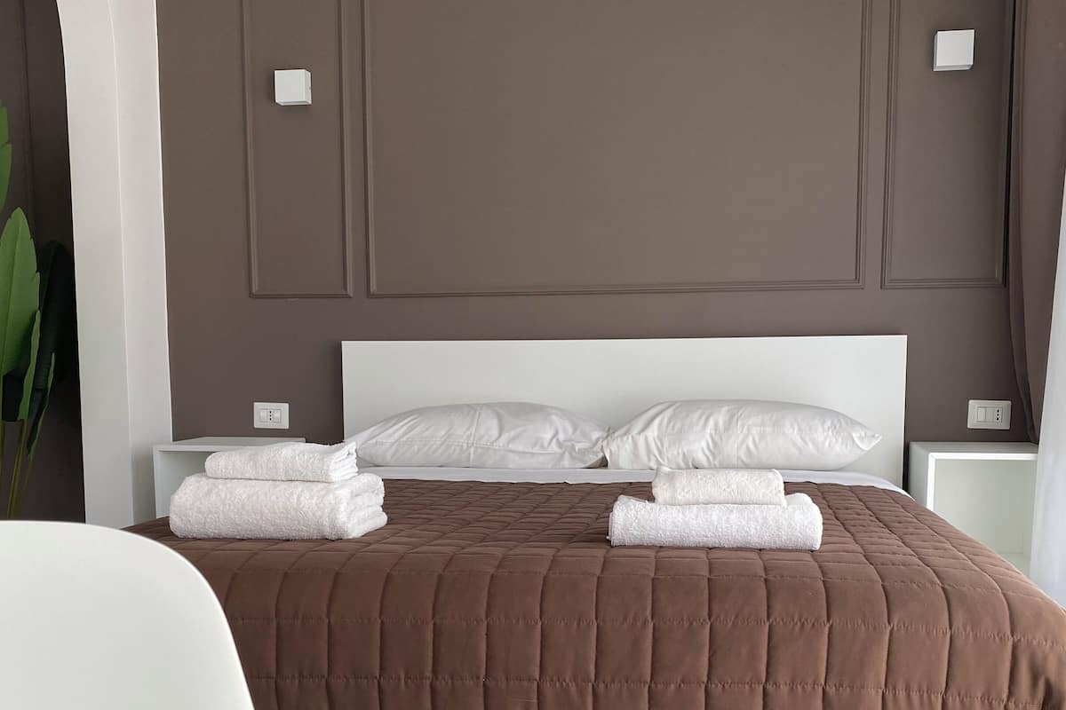 A neatly made bed with a brown quilt, white pillows, and folded white towels.
