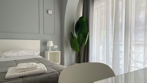 Une chambre d’hôtel moderne équipée d’un lit, d’une table de chevet, d’une lampe et d’une grande fenêtre avec des rideaux.