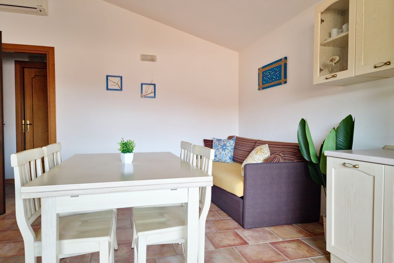 A dining area with a white table and chairs, a sofa with cushions, and a cabinet with glass doors.