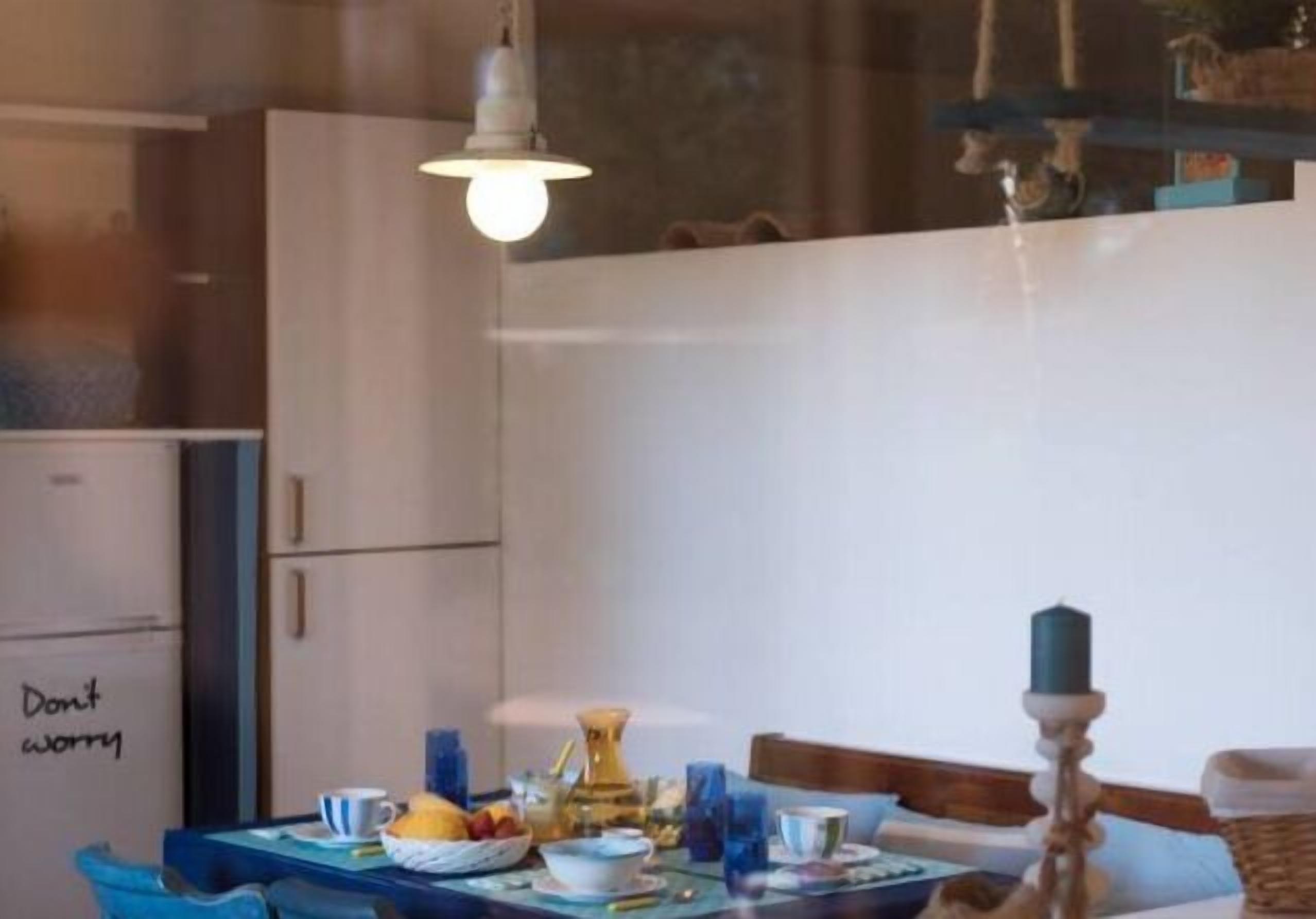 A dining area with a table set for two, a refrigerator with a note, and a hanging light fixture.