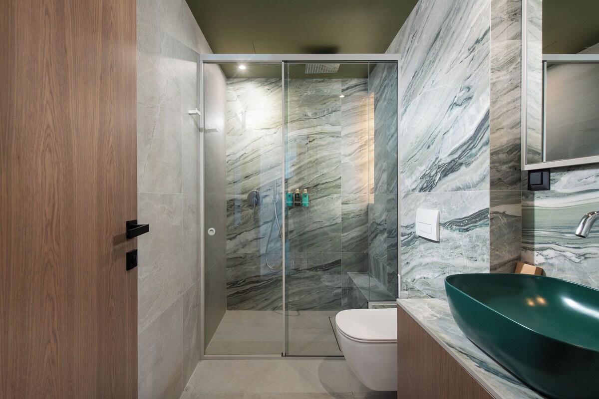 Un baño moderno con ducha envuelta en vidrio, un inodoro blanco y un lavamanos verde.