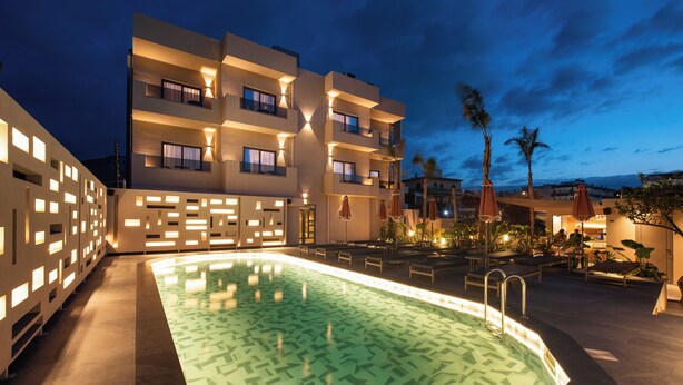 A pool area with a geometric tile pattern, a multi-story building with balconies, and outdoor seating with umbrellas.