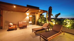 A modern outdoor lounge area with wooden furniture, a ceiling fan, and a view of the city at dusk.