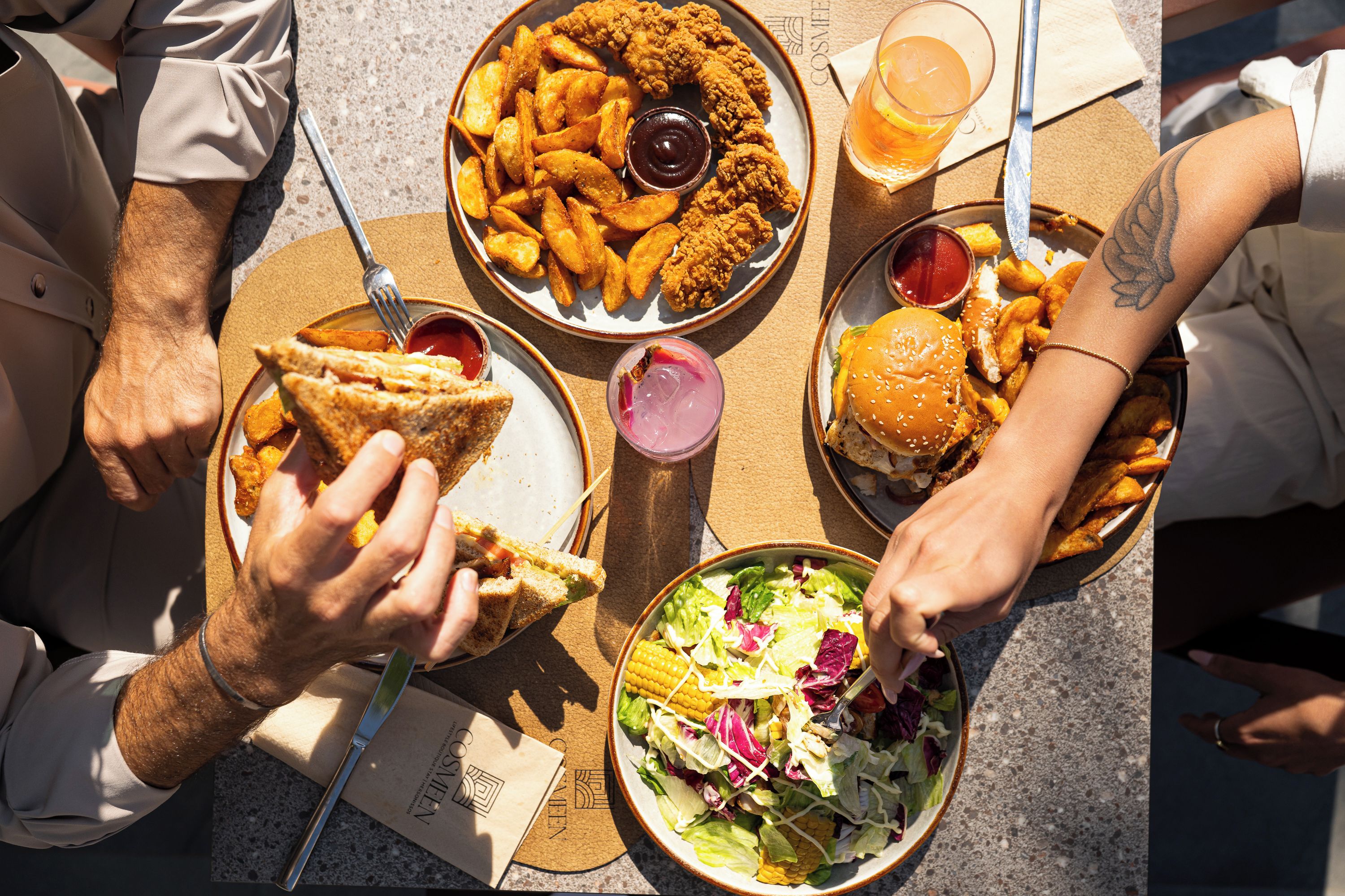 Un groupe de personnes est assis à une table et déguste différents plats, notamment un hamburger, des frites et une salade.