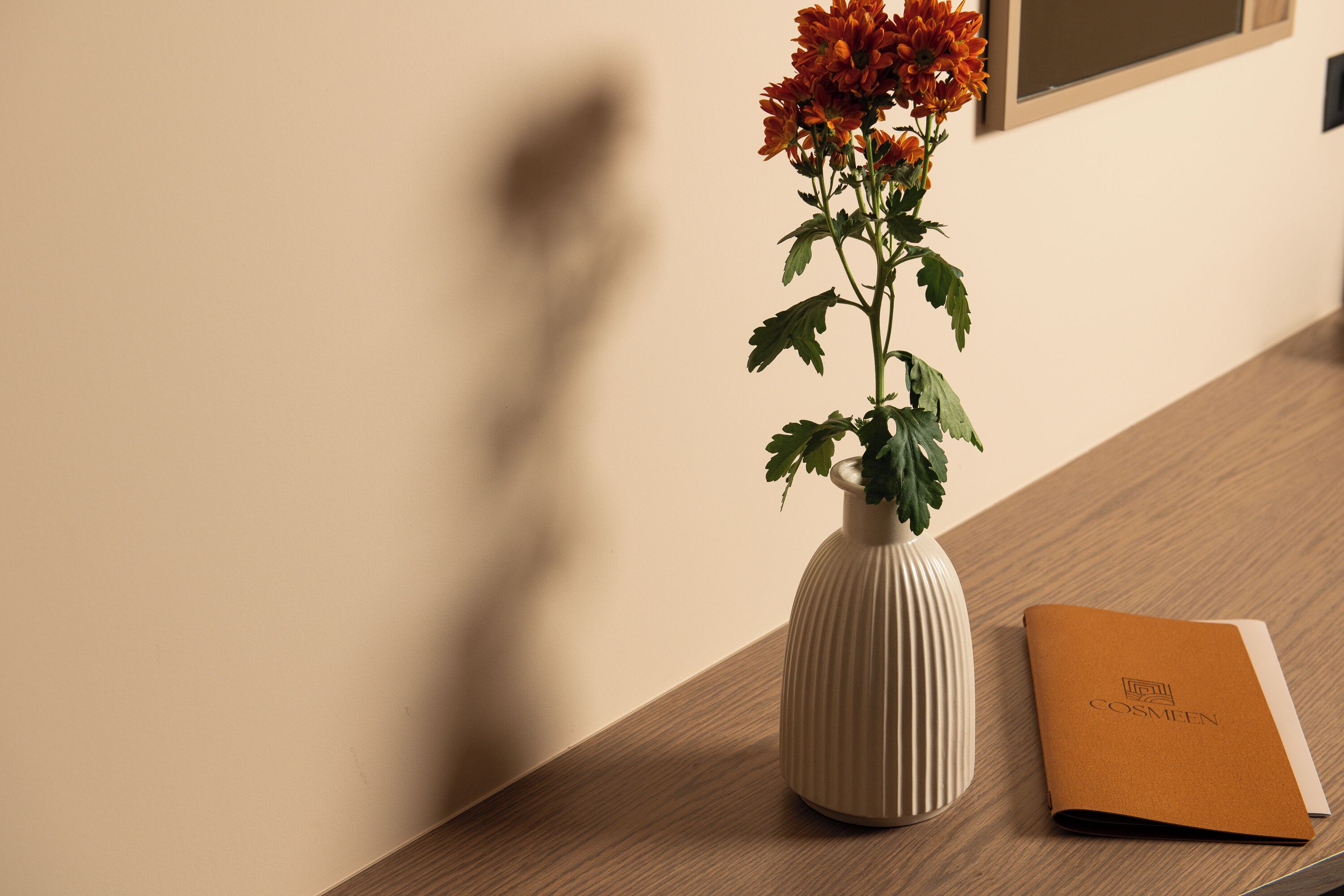 A wooden table with a white vase containing orange flowers and a brown booklet.