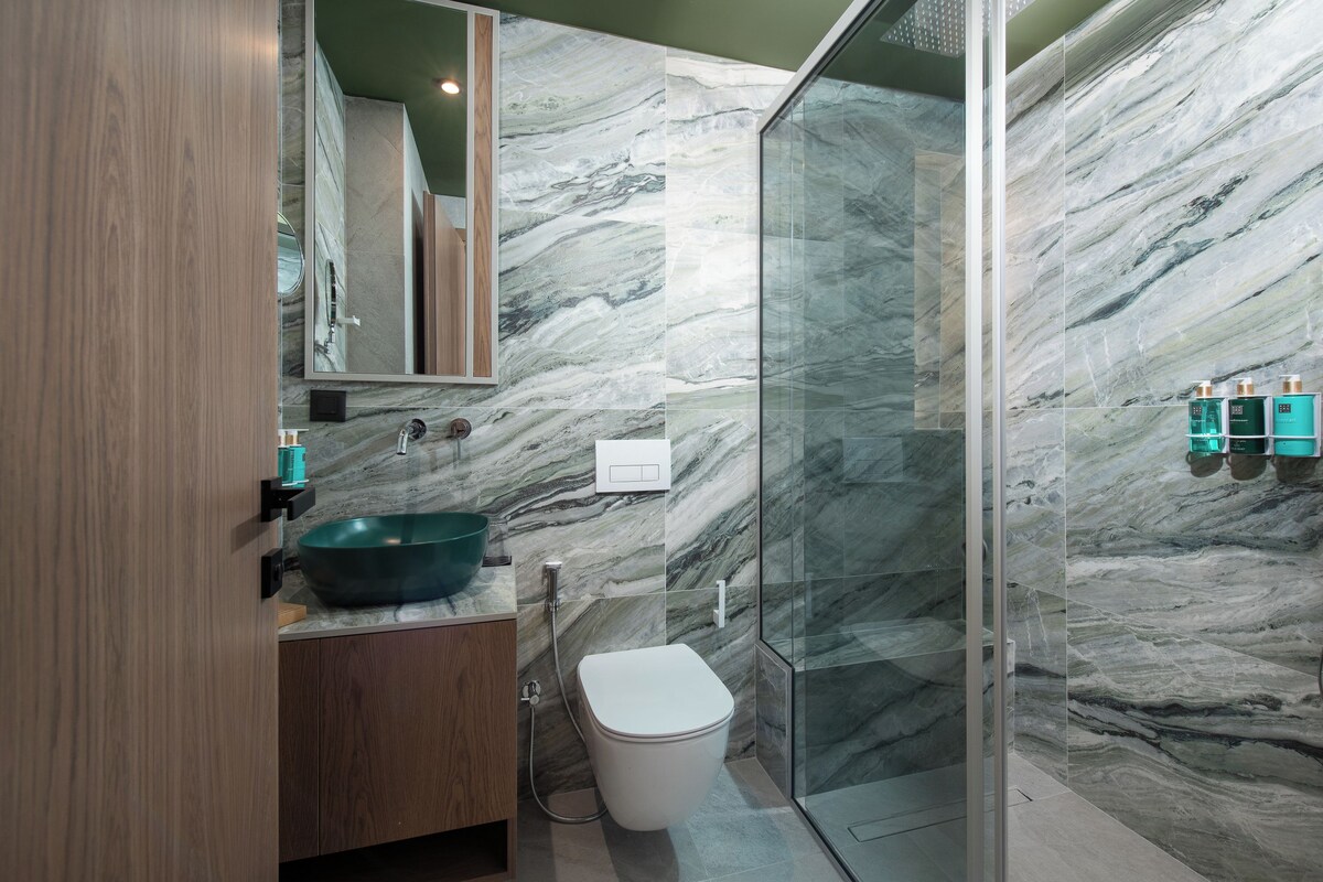 Ein modernes Badezimmer mit Marmorfliesenspiegel, einem Holzkosmetikschrank, einer Glasdusche und einer weißen Toilette.