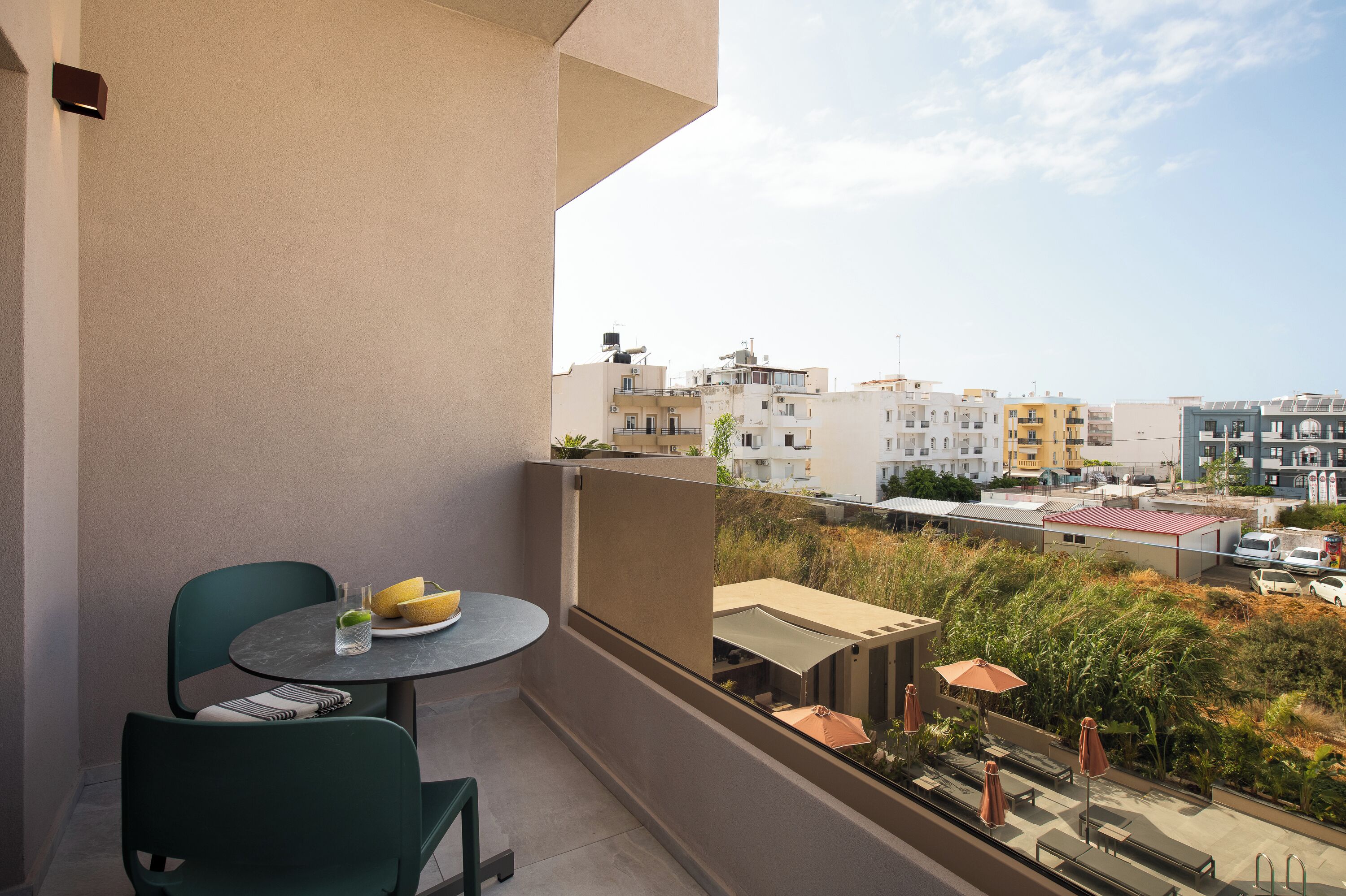 Een balkon met twee stoelen en een tafel, met uitzicht op een stadsgezicht met gebouwen en groen.