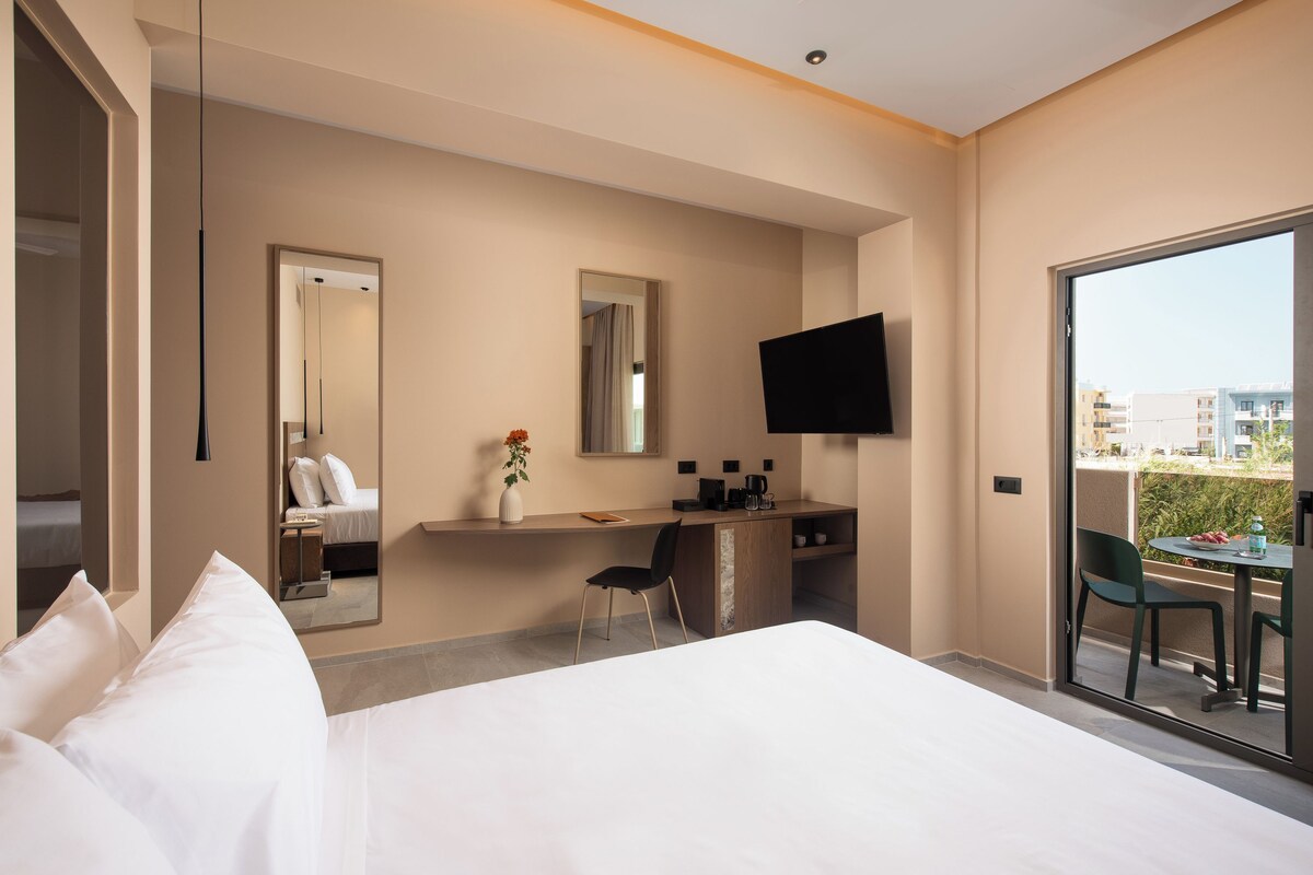 Ein Hotelzimmer mit einem Bett, einem Schreibtisch mit Stuhl, einem Fernseher und einem Balkon mit Tisch und Stühlen.