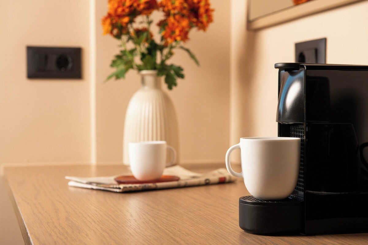Ein Holztisch mit einer weißen Kaffeetasse und einer schwarzen Kaffeemaschine.