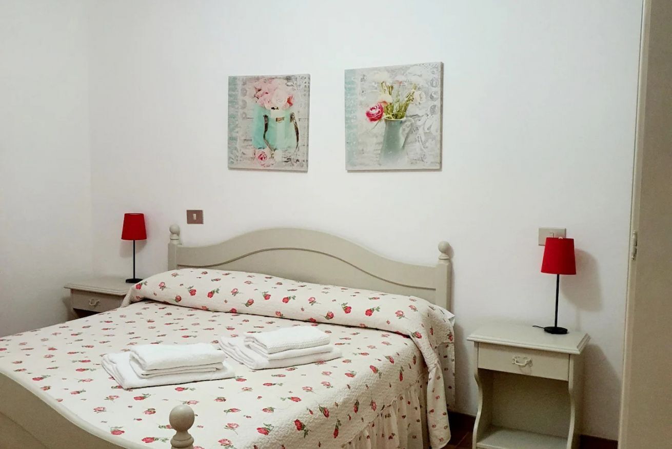 A neatly made bed with a floral bedspread, two bedside tables with lamps, and two wall-mounted paintings.