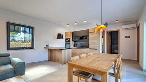 A modern kitchen with a wooden dining table and chairs, a built-in oven, and a large window overlooking a garden. - Villa Dreamview by Aneo Travel (Matulji)