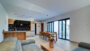 A modern living room with a sofa, a coffee table with a vase, and a dining area with chairs and a table. - Villa Dreamview by Aneo Travel (Matulji)