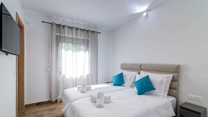 A hotel room with two beds, a flat-screen TV, a wooden floor, and a window with sheer curtains. - Villa Dreamview by Aneo Travel (Matulji)
