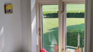 Una habitación con un escritorio blanco, una silla y un ventanal con vistas a un campo verde.