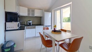 A compact kitchen with white cabinets, a coffee maker, and a dining area with a table and chairs.