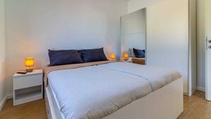 A modern bedroom with a large bed, two bedside tables with lamps, a wardrobe, and a mirror.