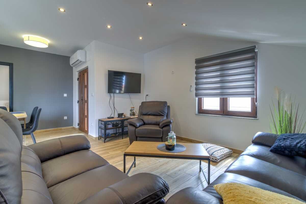 A modern living room with leather sofas, a wooden coffee table, a TV, and a large window with blinds.