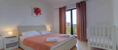 A bedroom with a bed, nightstands, a crib, a window with curtains, and an air conditioning unit.