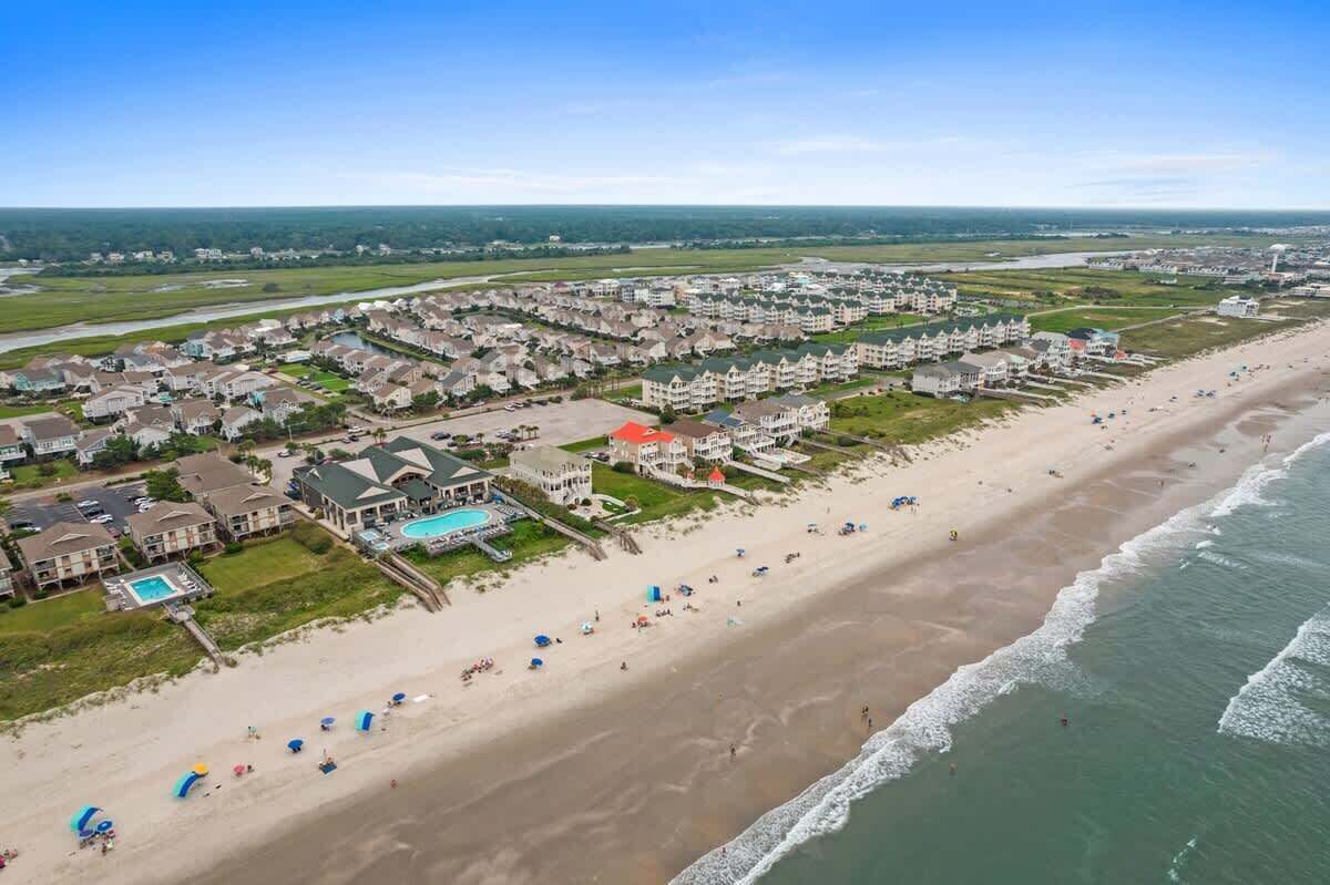 An aerial view of a coastal residential area with beachfront properties, a swimming pool, and a beach with umbrellas.
