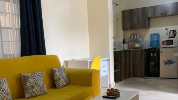 Een woonkamer met een gele bank, een witte salontafel en een keuken in de achtergrond.