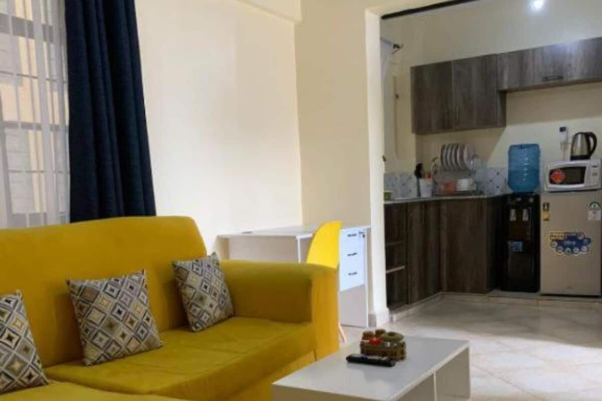 A living room with a yellow sofa, a white coffee table, and a kitchen area in the background.
