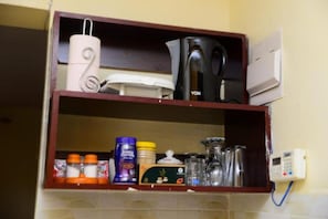 A kitchen shelf with a kettle, a coffee maker, and various kitchen items.