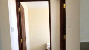 Een smalle gang met marmeren vloer, houten deuren en een klein trapje naar een badkamer.