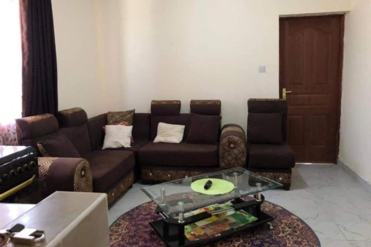 A living room with a sofa set, a glass coffee table, and a patterned rug.