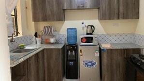 Een compacte keuken met houten kastjes, een spoelbak, een magnetron, een waterdispenser en een kleine koelkast.