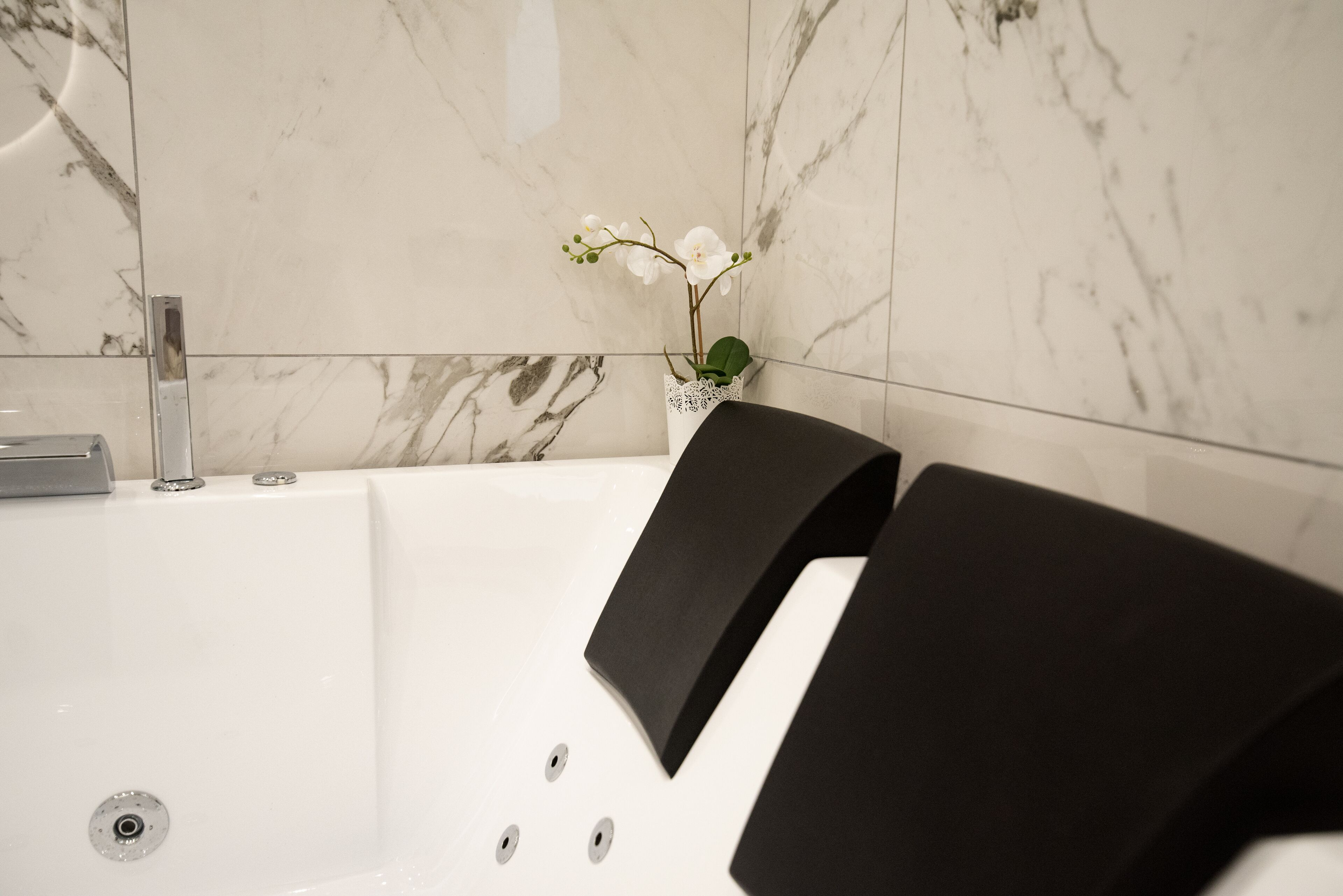 Et moderne badeværelse med en marmorvæg, et hvidt badekar og en hvid orchidé i en glasvase.