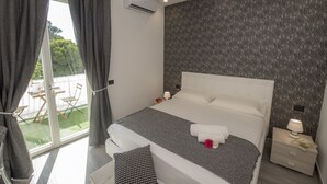 A bedroom with a large bed, a window with curtains, a patterned wall, and a small table with a lamp. - LA DOLCE VITA ROOMS (Procida)