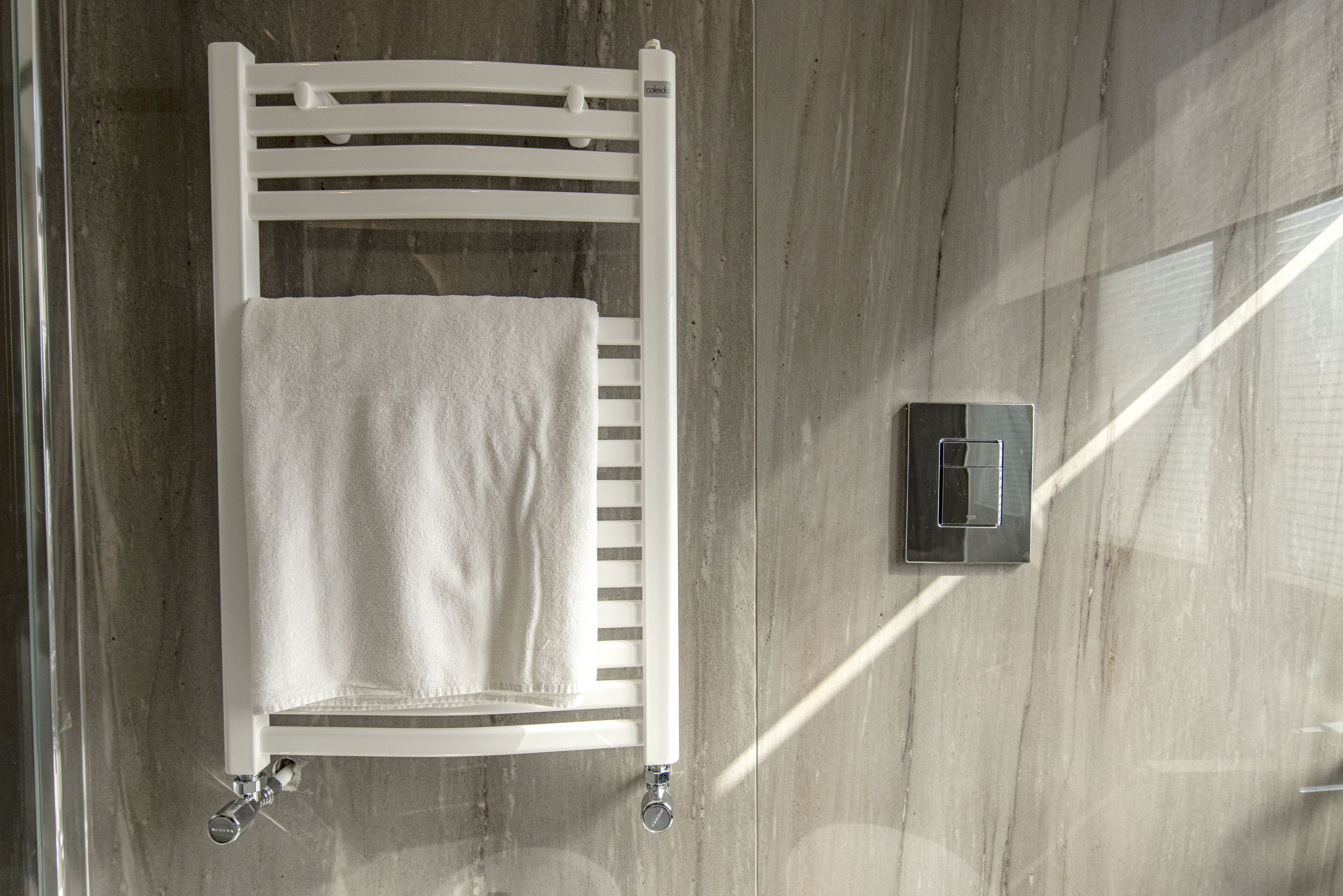 A white bed with a towel, a thermostat, and a water valve on a tiled floor.